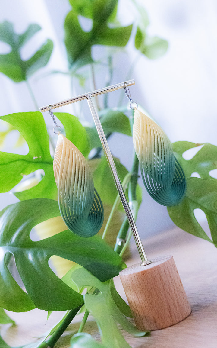 Boucles d’oreilles OASIS vert forêt dégradé ultralégères en nylon recyclé imprimé 3D présentées avec des feuilles tropicales signées Vox &amp; Oz