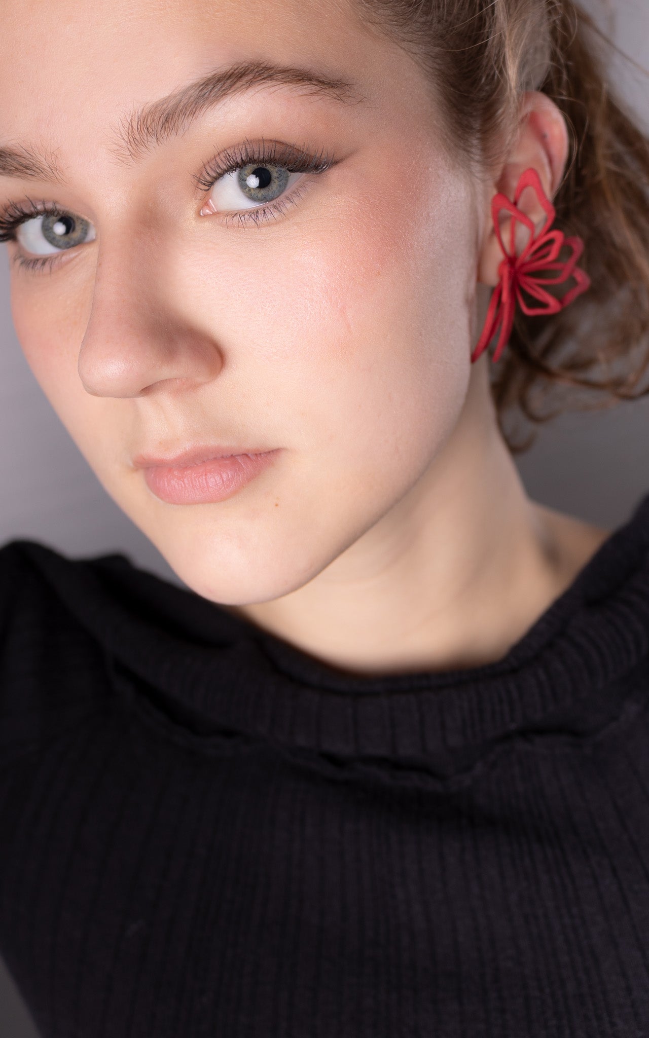 Jeune femme aux cheveux attachés avec jolie bijou rouge florale à l'oreille.