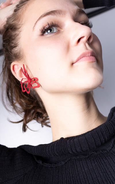 Jeune femme aux cheveux attachés avec jolie bijou rouge florale à l'oreille.